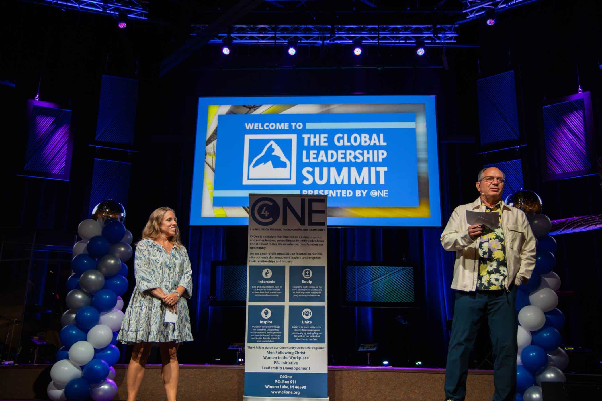 Man and woman standing on a stage with the C4One banner sign and Global Leadership Summit welcome slide behind them.